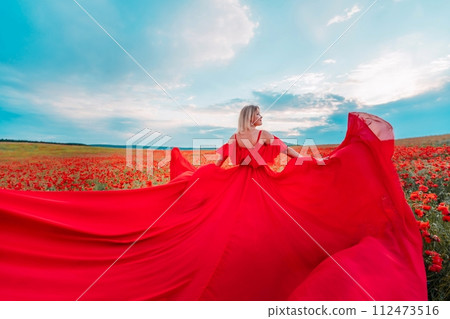 Woman poppy field red dress. Happy woman in a long red dress in a beautiful large poppy field. Blond stands with her back posing on a large field of red poppies 112473516