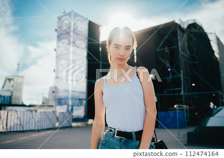 A woman is standing in front of a large building, wearing a white tank top A woman is standing in front of a large building, wearing a white tank top 112474164
