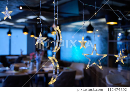 In a modern restaurant, the ambiance is transformed by the presence of sparkling Islamic symbolic Ramadan decorations, creating a festive and culturally rich atmosphere In a modern restaurant, the ambiance is transformed by the presence of sparkling Islamic symbolic Ramadan decorations, creating a festive and culturally rich atmosphere 112474892