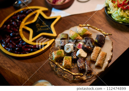 In this captivating aerial view, delicious food adorned with Ramadan decorations, including dates and meat, awaits the arrival of an European Islamic family, promising a festive and flavorful iftar In this captivating aerial view, delicious food adorned with Ramadan decorations, including dates and meat, awaits the arrival of an European Islamic family, promising a festive and flavorful iftar 112474899