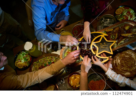 In this modern portrayal, a European Islamic family partakes in the tradition of breaking their Ramadan fast with dates, symbolizing unity, cultural heritage, and spiritual observance during the holy In this modern portrayal, a European Islamic family partakes in the tradition of breaking their Ramadan fast with dates, symbolizing unity, cultural heritage, and spiritual observance during the holy 112474901
