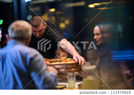 In a heartwarming scene, a professional chef serves an European Muslim family their iftar meal during the holy month of Ramadan, embodying cultural unity and culinary hospitality in a moment of shared 112474928