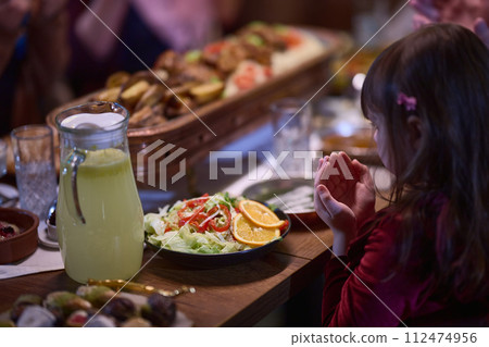 A young girl raises her hands in prayer as she prepares for her iftar meal during the holy month of Ramadan, embodying spiritual devotion and innocence. A young girl raises her hands in prayer as she prepares for her iftar meal during the holy month of Ramadan, embodying spiritual devotion and innocence. 112474956