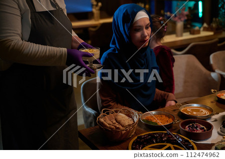 In a heartwarming scene, a professional chef serves an European Muslim family their iftar meal during the holy month of Ramadan, embodying cultural unity and culinary hospitality in a moment of shared In a heartwarming scene, a professional chef serves an European Muslim family their iftar meal during the holy month of Ramadan, embodying cultural unity and culinary hospitality in a moment of shared 112474962