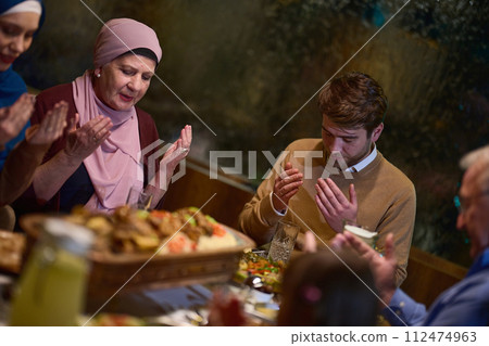 In a modern restaurant setting, a European Islamic family comes together for iftar during Ramadan, engaging in prayer before the meal, uniting tradition and contemporary practices in a celebration of 112474963