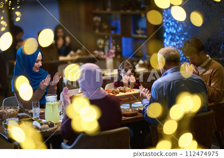 In a modern restaurant setting, a European Islamic family comes together for iftar during Ramadan, engaging in prayer before the meal, uniting tradition and contemporary practices in a celebration of In a modern restaurant setting, a European Islamic family comes together for iftar during Ramadan, engaging in prayer before the meal, uniting tradition and contemporary practices in a celebration of 112474975