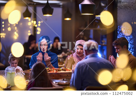 In a modern restaurant setting, a European Islamic family comes together for iftar during Ramadan, engaging in prayer before the meal, uniting tradition and contemporary practices in a celebration of In a modern restaurant setting, a European Islamic family comes together for iftar during Ramadan, engaging in prayer before the meal, uniting tradition and contemporary practices in a celebration of 112475002