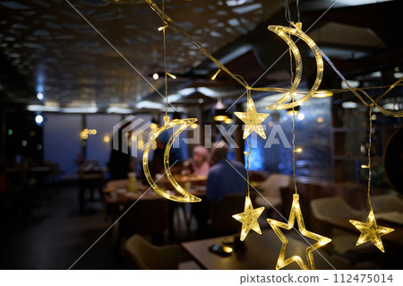 In a modern restaurant, the ambiance is transformed by the presence of sparkling Islamic symbolic Ramadan decorations, creating a festive and culturally rich atmosphere In a modern restaurant, the ambiance is transformed by the presence of sparkling Islamic symbolic Ramadan decorations, creating a festive and culturally rich atmosphere 112475014