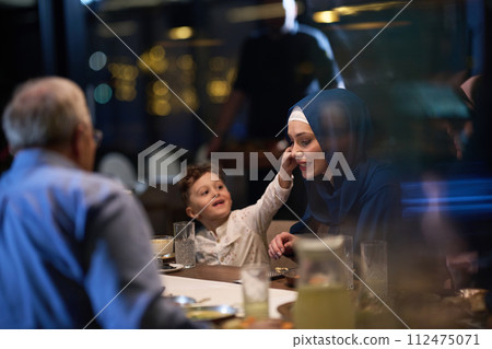 In a heartwarming scene, a happy European Islamic family and a young girl delightfully engage with her mother while eagerly anticipating their iftar meal, radiating joy, love, and familial bonding 112475071