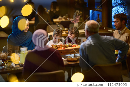 A modern and traditional European Islamic family comes together for iftar in a contemporary restaurant during the Ramadan fasting period, embodying cultural harmony and familial unity amidst a A modern and traditional European Islamic family comes together for iftar in a contemporary restaurant during the Ramadan fasting period, embodying cultural harmony and familial unity amidst a 112475093