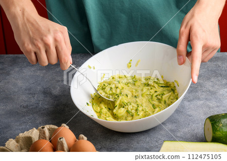 Female hands mixing with fork beaten eggs and grated zucchini in a glass bowl Female hands mixing with fork beaten eggs and grated zucchini in a glass bowl 112475105