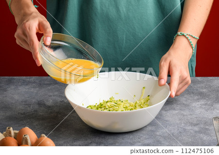 woman hands cooking omelette with grated zucchini, add a beaten eggs into bowl with grated zucchini woman hands cooking omelette with grated zucchini, add a beaten eggs into bowl with grated zucchini 112475106