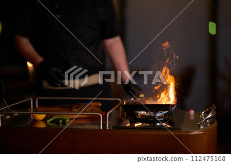 Close-up shot, a professional chef expertly prepares a delicious steak using modern cooking techniques, showcasing culinary excellence and precision in the art of gourmet cuisine 112475108
