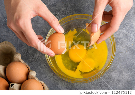Woman's hands cracking fresh egg, yolk and white dropping in a bowl, top view 112475112