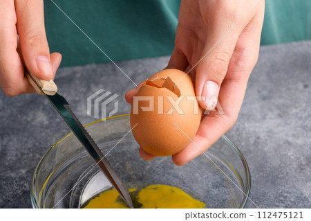 A cracked egg in the hand, close up. A woman's hand cracking an egg with knife A cracked egg in the hand, close up. A woman's hand cracking an egg with knife 112475121