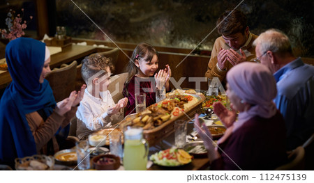 In a modern restaurant setting, a European Islamic family comes together for iftar during Ramadan, engaging in prayer before the meal, uniting tradition and contemporary practices in a celebration of In a modern restaurant setting, a European Islamic family comes together for iftar during Ramadan, engaging in prayer before the meal, uniting tradition and contemporary practices in a celebration of 112475139