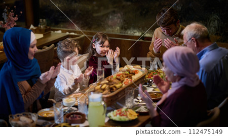 In a modern restaurant setting, a European Islamic family comes together for iftar during Ramadan, engaging in prayer before the meal, uniting tradition and contemporary practices in a celebration of In a modern restaurant setting, a European Islamic family comes together for iftar during Ramadan, engaging in prayer before the meal, uniting tradition and contemporary practices in a celebration of 112475149