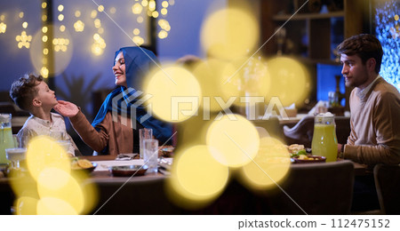 In a modern restaurant, an Islamic couple and their children joyfully await their iftar meal during the holy month of Ramadan, embodying familial harmony and cultural celebration amidst the 112475152
