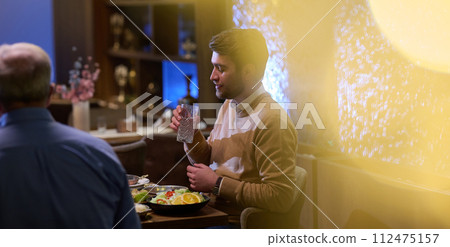 A son and his elderly father engage in heartfelt conversation while patiently awaiting their iftar meal, fostering intergenerational bonding and cherished moments of family connection 112475157