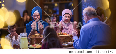 In a modern restaurant setting, a European Islamic family comes together for iftar during Ramadan, engaging in prayer before the meal, uniting tradition and contemporary practices in a celebration of 112475169