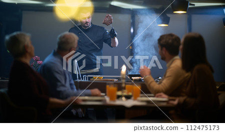 In a restaurant setting, a professional chef presents a sizzling steak cooked over an open flame, while an European Muslim family eagerly awaits their iftar meal during the holy month of Ramadan 112475173