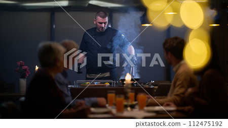 In a restaurant setting, a professional chef presents a sizzling steak cooked over an open flame, while an European Muslim family eagerly awaits their iftar meal during the holy month of Ramadan 112475192