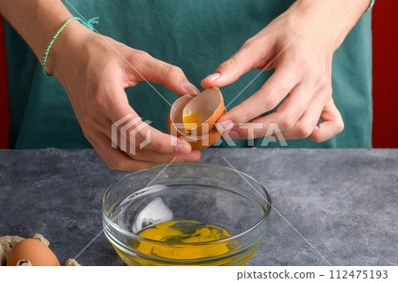 A woman's hand holding the eggshells of breked egg into a clear glass bowl in the gray kitchen table A woman's hand holding the eggshells of breked egg into a clear glass bowl in the gray kitchen table 112475193