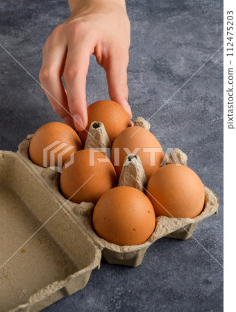 Female hand selected an egg in egg box on gray background, close up 112475203