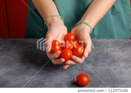 Woman holding ripe tomatoes cherry in her hands at gray table background, close up Woman holding ripe tomatoes cherry in her hands at gray table background, close up 112475206
