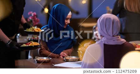 A modern and traditional European Islamic family comes together for iftar in a contemporary restaurant during the Ramadan fasting period, embodying cultural harmony and familial unity amidst a A modern and traditional European Islamic family comes together for iftar in a contemporary restaurant during the Ramadan fasting period, embodying cultural harmony and familial unity amidst a 112475209