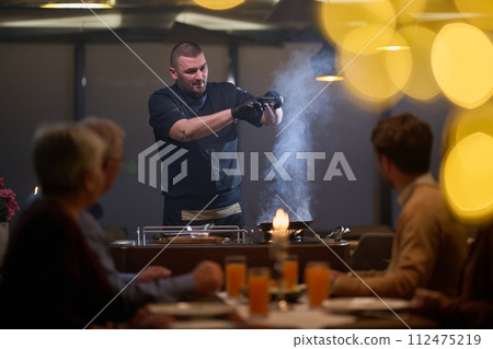 In a restaurant setting, a professional chef presents a sizzling steak cooked over an open flame, while an European Muslim family eagerly awaits their iftar meal during the holy month of Ramadan 112475219