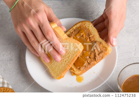 Female hands making a sandwich with honey and peanut butter spreading on piece of white bread Female hands making a sandwich with honey and peanut butter spreading on piece of white bread 112475238