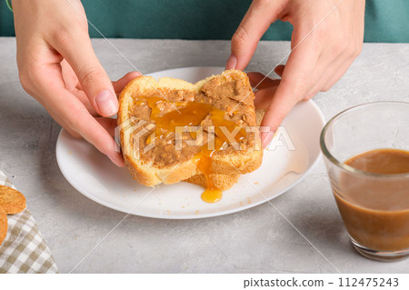 Female hands holding a sandwich with honey and peanut butter spreading on piece of white bread 112475243