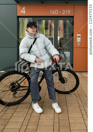 A man in a cap stands with a bicycle in the courtyard of a house 112475533