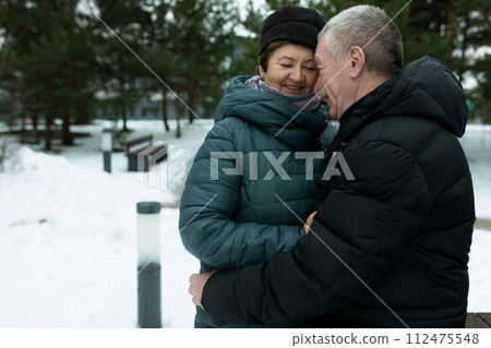 Cute mature couple experiencing love for each other while walking in the park in winter Cute mature couple experiencing love for each other while walking in the park in winter 112475548