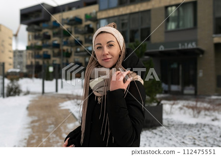 Well-groomed young woman dressed in a winter black coat with a scarf in an urban environment 112475551