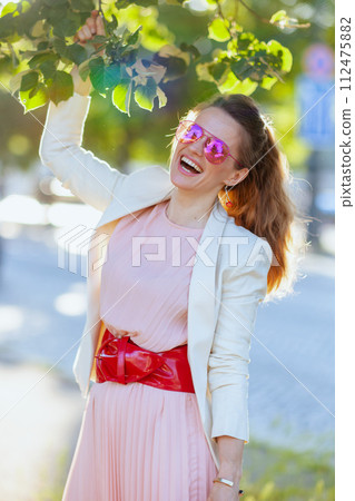 happy trendy woman in pink dress and white jacket in city 112475882