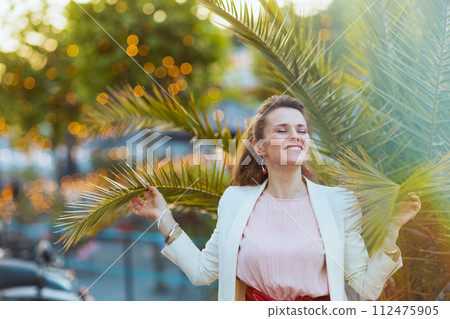 smiling stylish woman in pink dress and white jacket in city 112475905