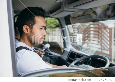 Man driver and mover in a truck for relocation service. Teamwork in transporting and delivering furniture. Smiling employees working confidently. House moving service concept. Man driver and mover in a truck for relocation service. Teamwork in transporting and delivering furniture. Smiling employees working confidently. House moving service concept. 112476029