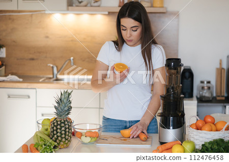 Attractive woman holds a piece of orange in her hands and sniffs it. A full table of fruits and vegetables. Squeezer Attractive woman holds a piece of orange in her hands and sniffs it. A full table of fruits and vegetables. Squeezer 112476458