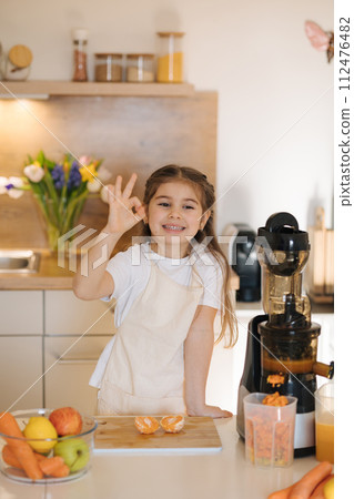 Portrait of cute five year old girl in apron preparing organic fruits and vegetables for fresh juice. Homemade vegan beverage from juicer Portrait of cute five year old girl in apron preparing organic fruits and vegetables for fresh juice. Homemade vegan beverage from juicer 112476482