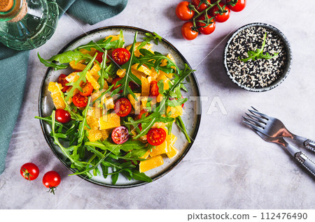 Homemade salad of orange, cherry tomatoes and arugula on a plate on the table top view 112476490