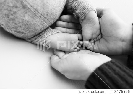 The palms of the father, the mother are holding the foot of the newborn baby. Feet of the newborn on the palms of the parents. Studio macro black and white photo of a child's toes, heels and feet.  The palms of the father, the mother are holding the foot of the newborn baby. Feet of the newborn on the palms of the parents. Studio macro black and white photo of a child's toes, heels and feet.  112476596
