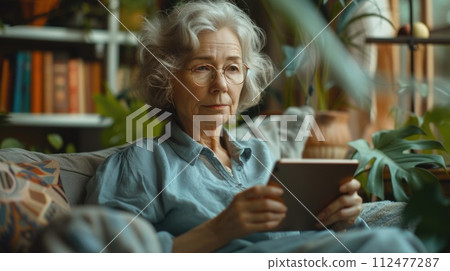 AI-generated content. An elderly woman sitting on a couch while holding a tablet device. 112477287
