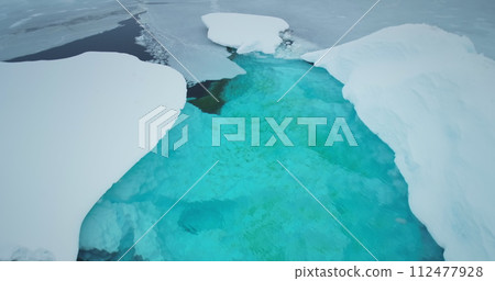 Melting arctic blue water glaciers aerial view. Snow covered iceberg with melted turquoise hole inside. Polar climate change. Arctic winter landscape, global warming problem. Close up drone flight Melting arctic blue water glaciers aerial view. Snow covered iceberg with melted turquoise hole inside. Polar climate change. Arctic winter landscape, global warming problem. Close up drone flight 112477928
