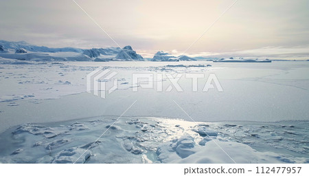 Fly over frozen Antarctic ocean sunset landscape. Snow covered untouched wilderness of South Pole. Desert white land of snow and ice aerial drone shot. Mountains in background. Nature conservation Fly over frozen Antarctic ocean sunset landscape. Snow covered untouched wilderness of South Pole. Desert white land of snow and ice aerial drone shot. Mountains in background. Nature conservation 112477957