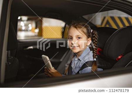 Happy little girl sitting on back seat of modern car in child chair. 112478179