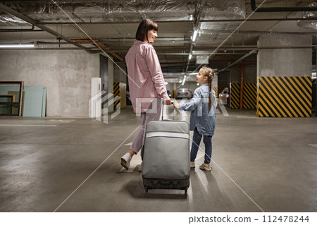 Caucasian mom and her small daughter walking through underground parking lot. 112478244