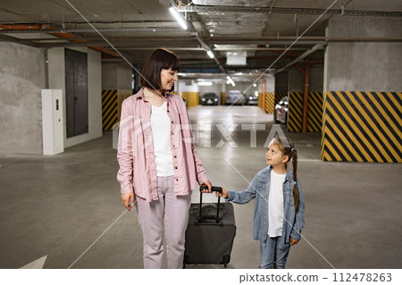 Young woman with child holding traveling suitcase as searching for car. 112478263