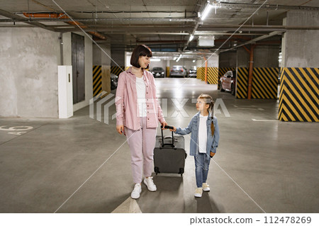 Caucasian mother and little daughter walking through underground parking lot. 112478269